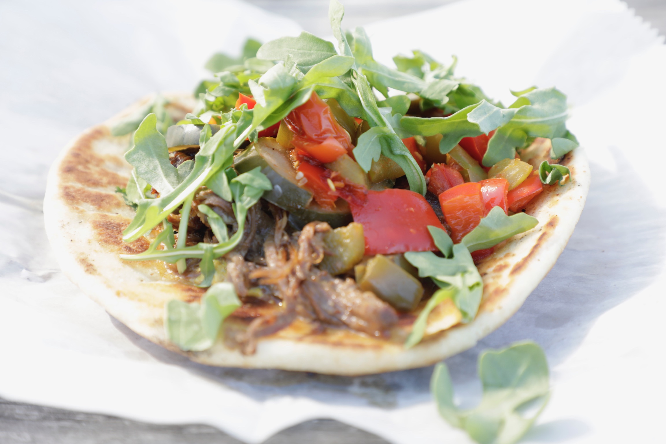 Pulled meat on flatbread with arugula, roasted red peppers and onion
