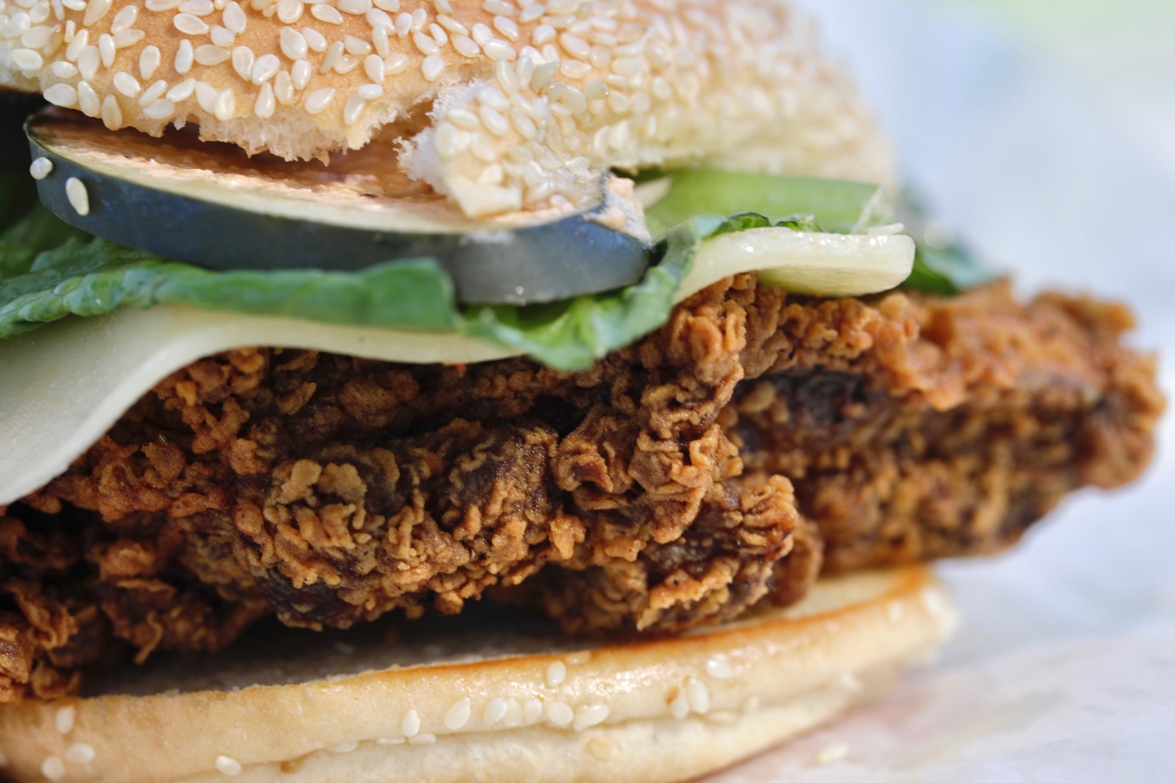 Fried chicken sandwich topped with avocado on a sesame seed bun