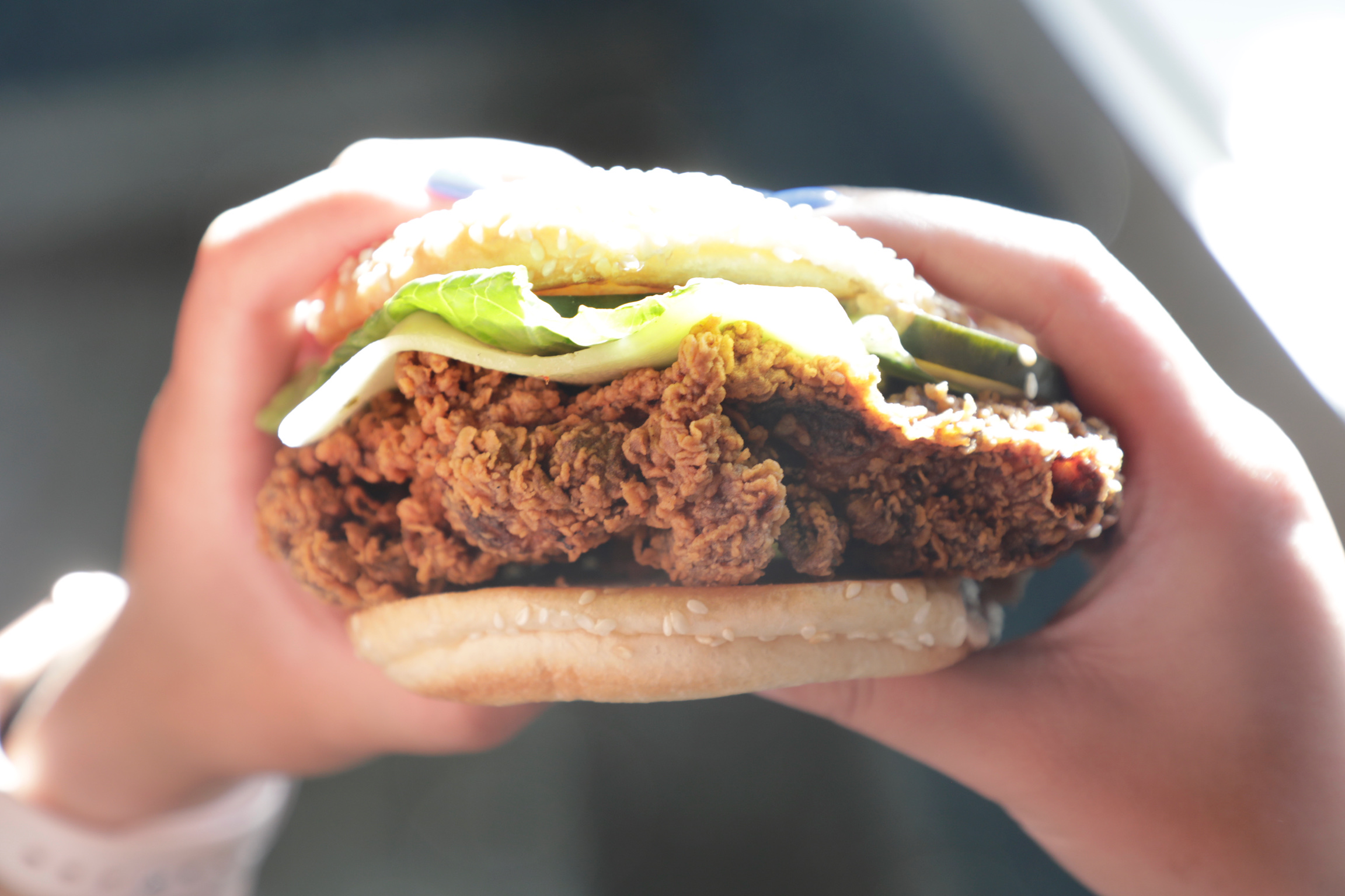 Buttermilk fried chicken sandwich with pickles and lettuce, held in hand