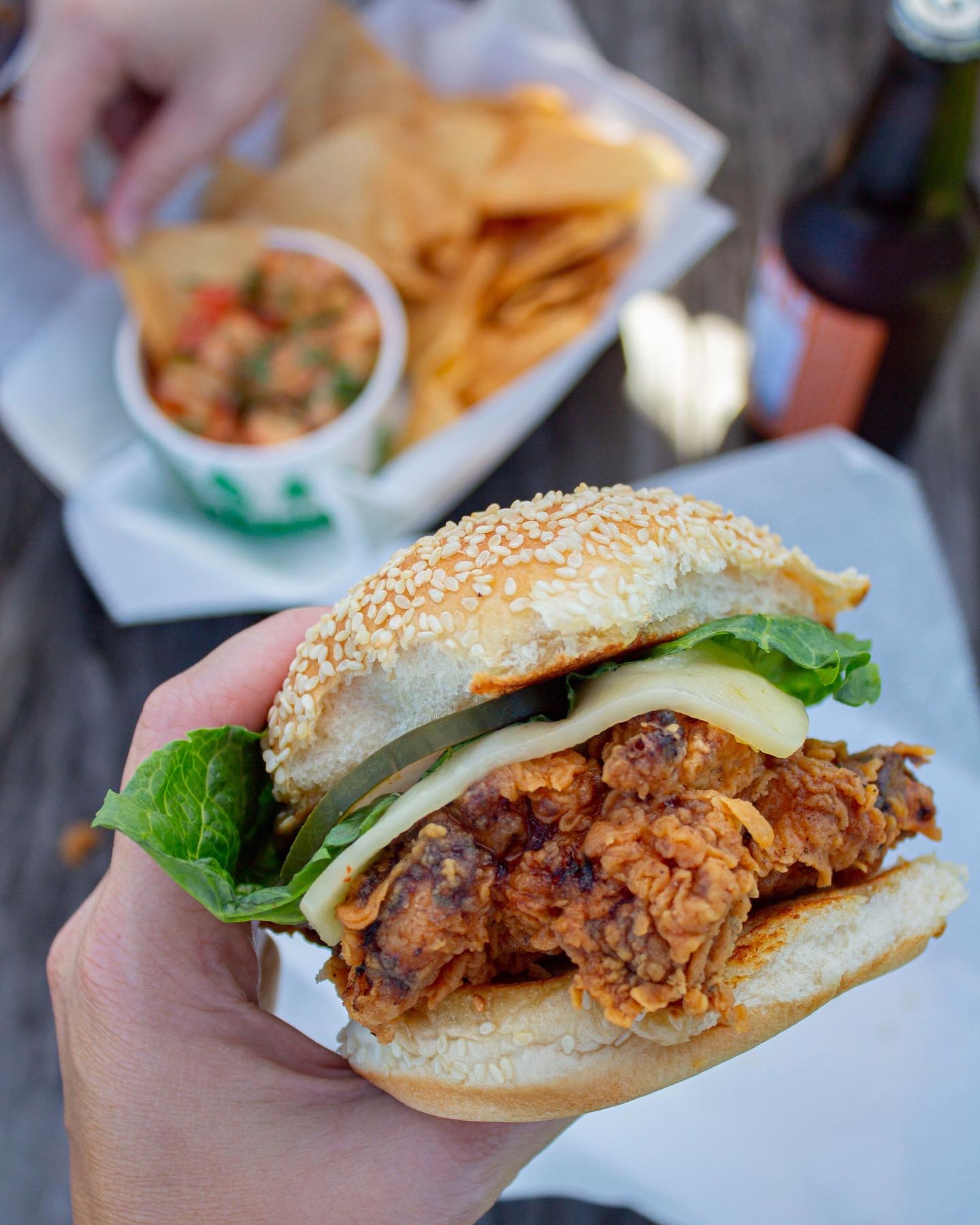 Pulled chicken sandwich held in hand with a basket of fries behind it