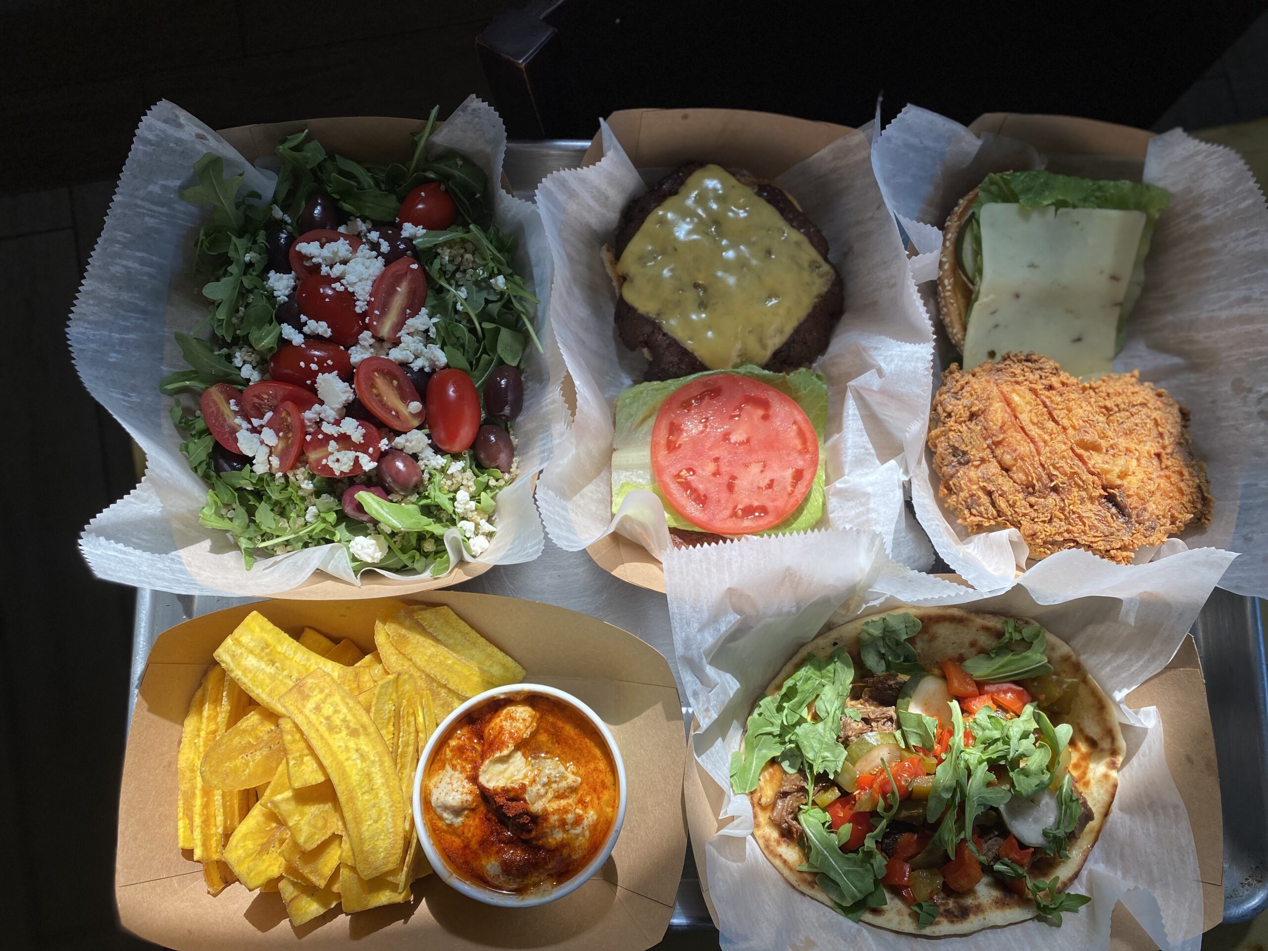 Takeout containers of tomato salad, dips, plantain chips and rice