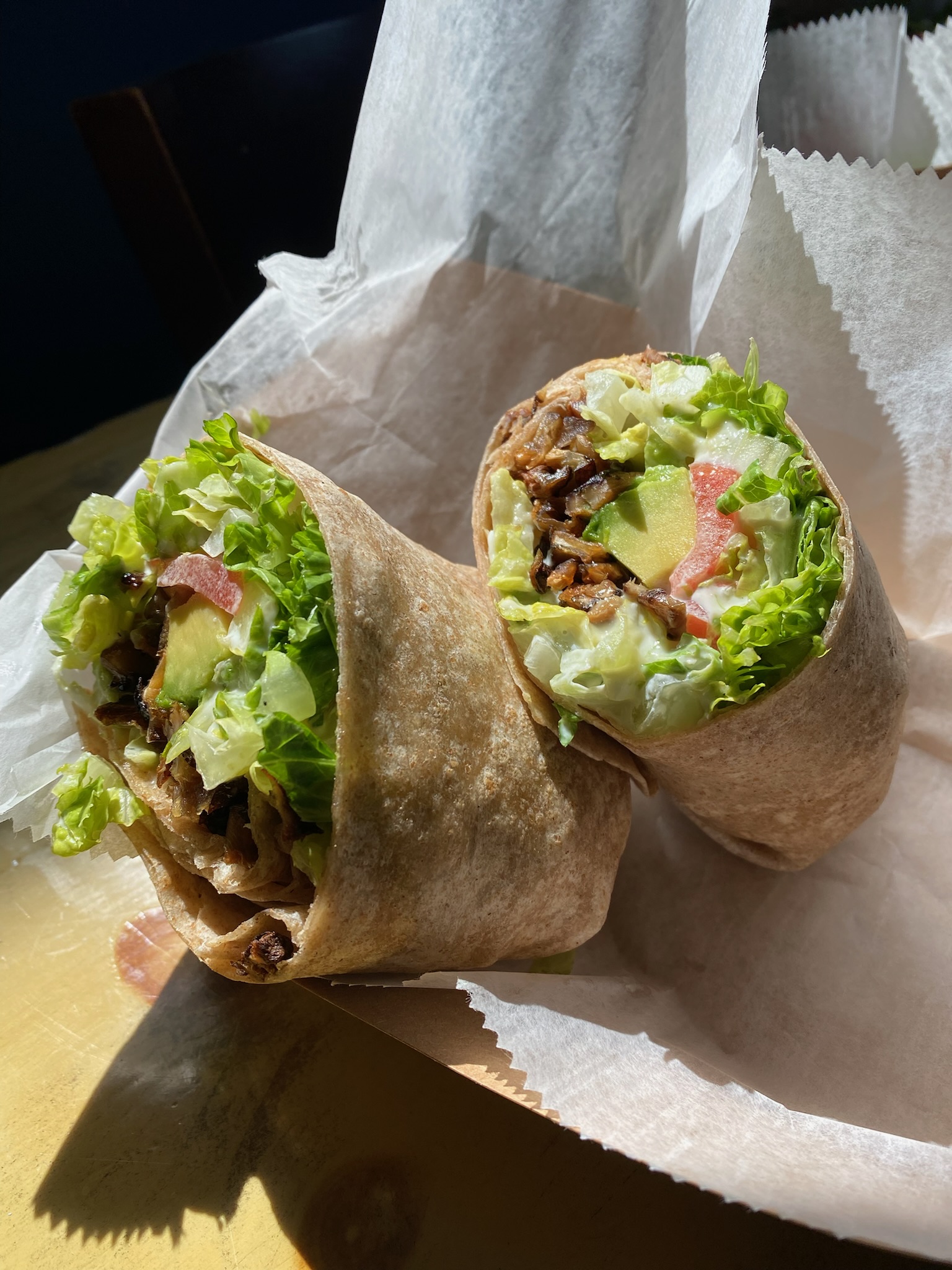 Two wraps in paper filled with lettuce, avocado and pickled vegetables
