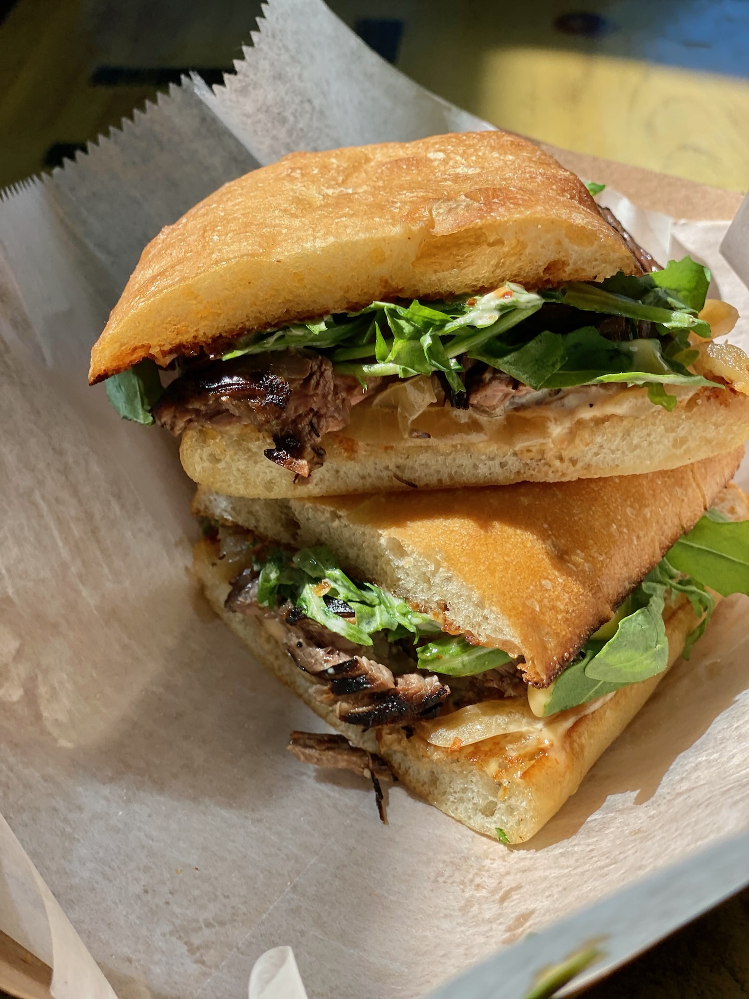 Marinated steak sandwich on ciabatta with caramelized onion and arugula