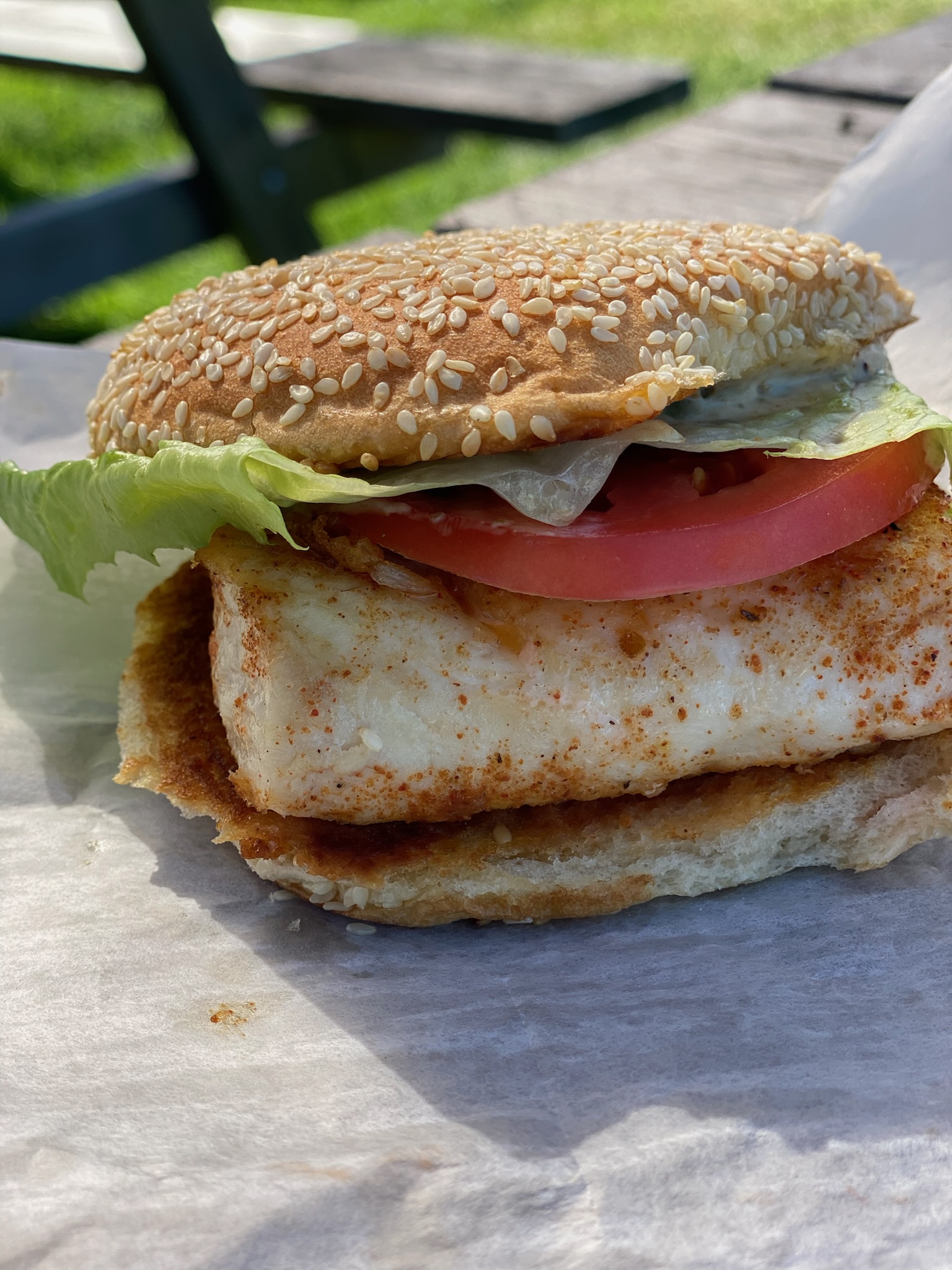 Fish sandwich on a sesame bun with tomato, lettuce and tartar sauce