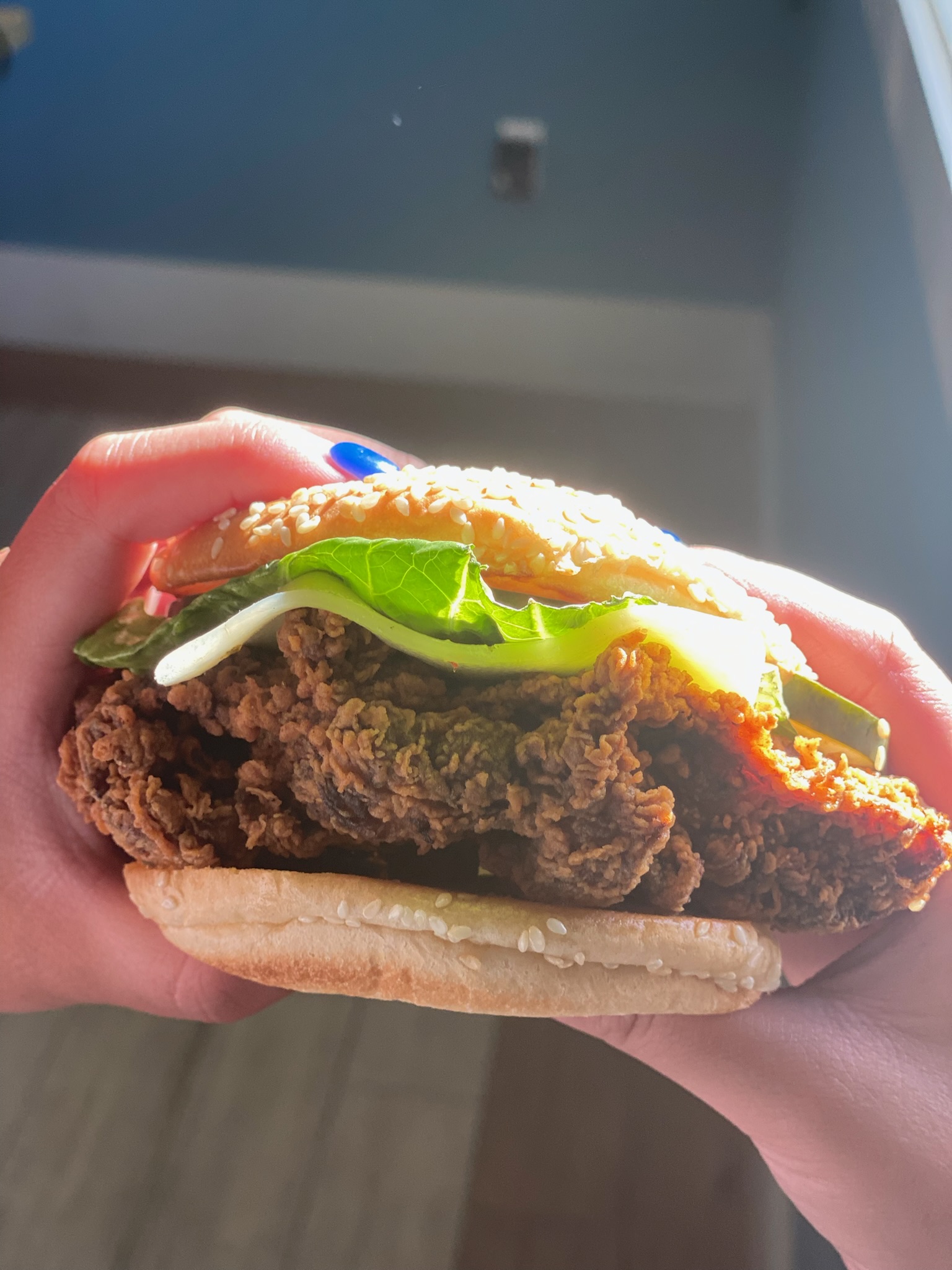 Fried chicken sandwich with avocado and lettuce, held in hand