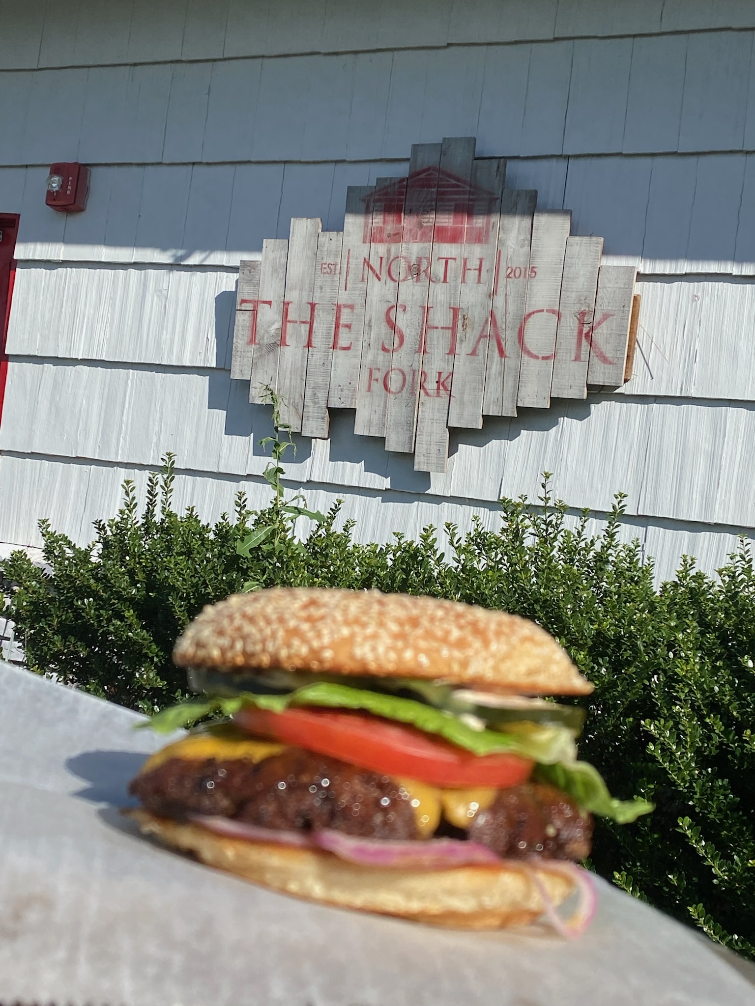 Burger held up in front of the carved North Fork Shack sign