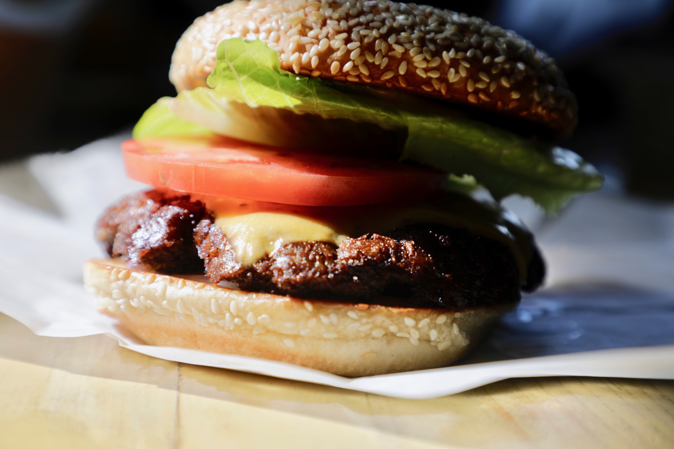 Burger stacked with avocado, tomato, lettuce and melted cheese on a sesame bun