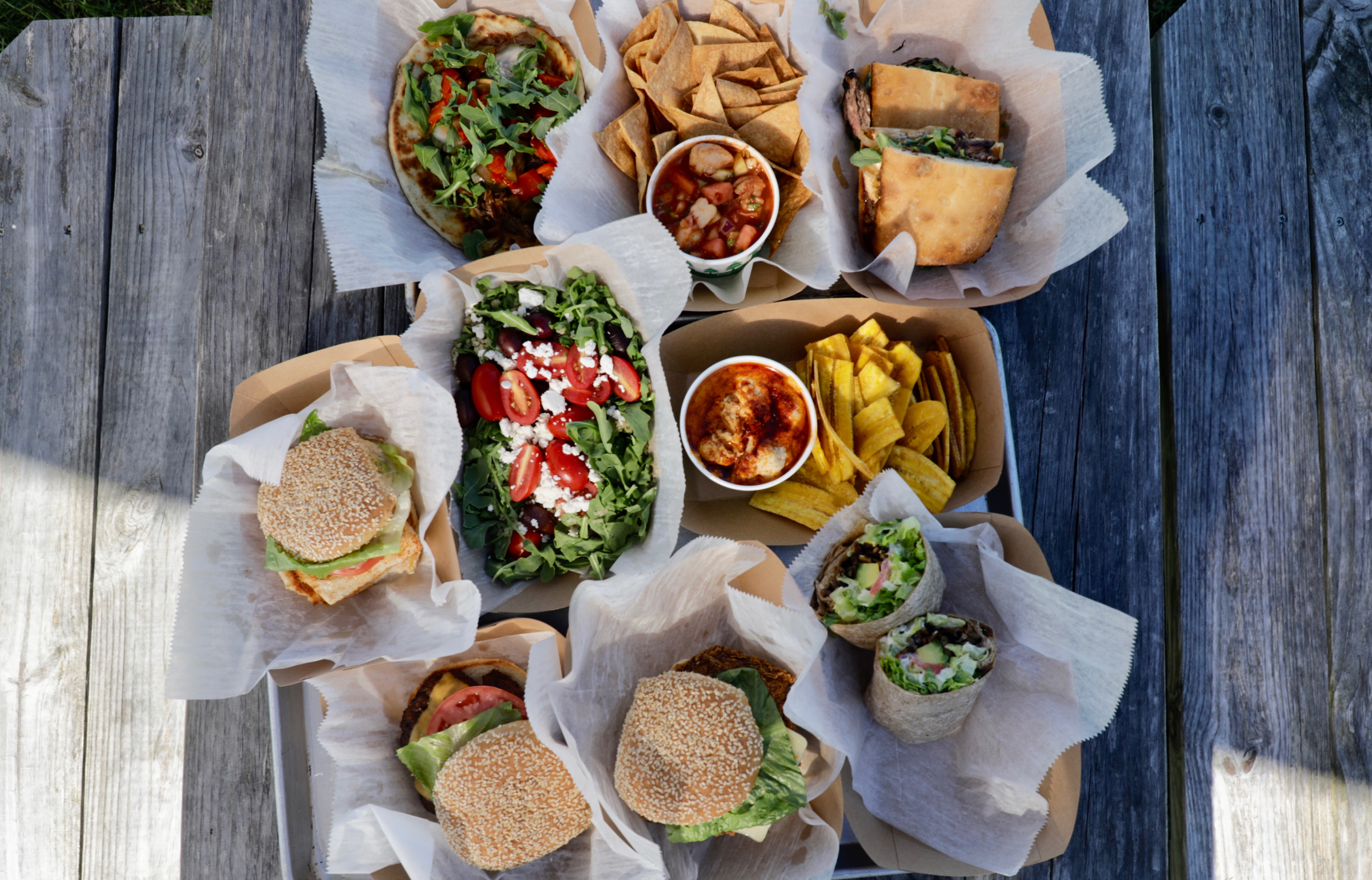 Overhead spread of sandwiches, salads, dips and sides in takeout containers